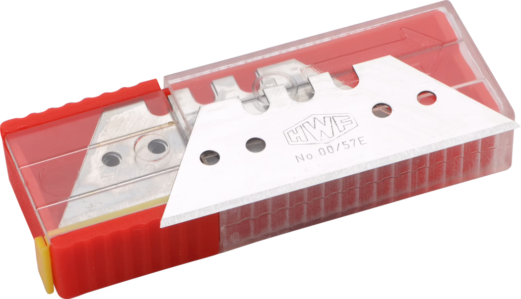 Pajarito_Dummy_Trapezoid blades Easy Line_034956_2021-02 Nahaufnahme einer Packung Ersatzklingen für Cuttermesser in einem rechteckigen roten Kunststoffspender mit durchsichtigem Deckel. Eine einzelne silberne Metallklinge mit Prägung 'HWF No.00/57E' liegt teilweise außerhalb des Behälters und zeigt ihre scharfe abgeschrägte Schneide und runde Montageöffnungen. Die rote Basis hat eine strukturierte Grifffläche und einen gelben Endverschluss. Der transparente Kunststoffdeckel gibt weitere gestapelte Klingen im Inneren frei. Studio-Beleuchtung betont den metallischen Glanz und die feine Schneide.