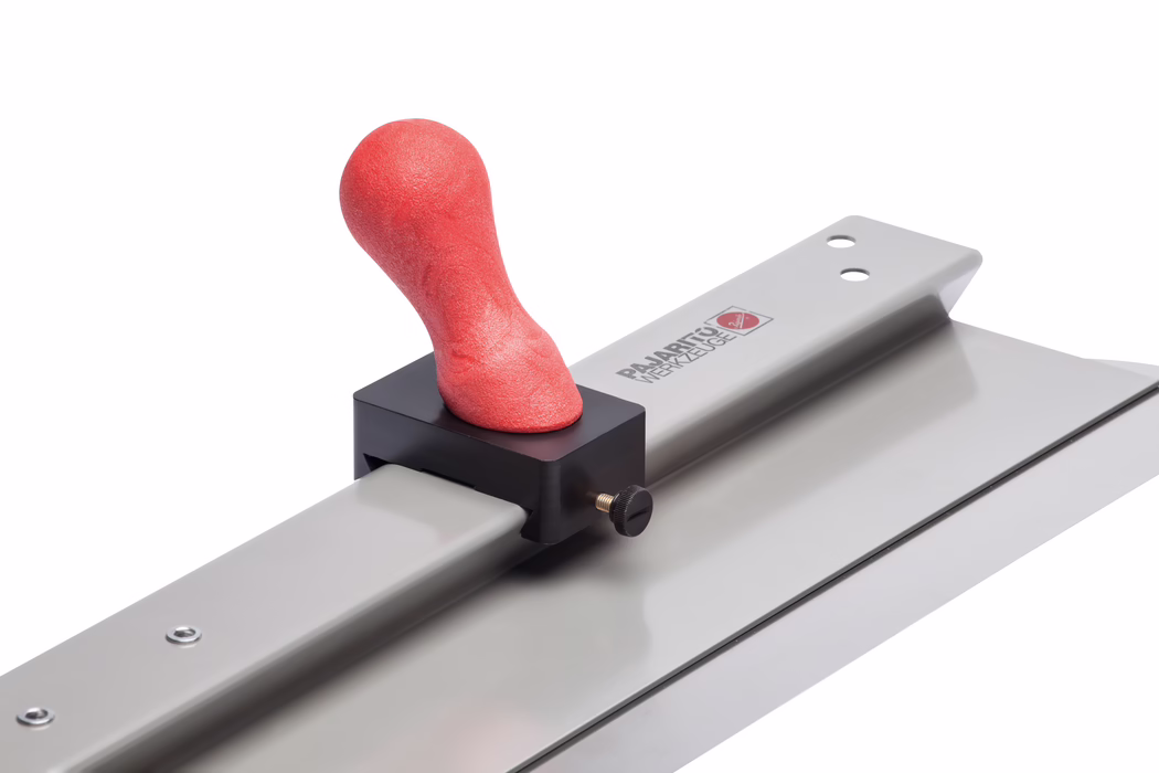Nahaufnahme einer Metall-Glättkelle mit langer rechteckiger, flacher Klinge, die auf einer Metallschiene montiert ist; ein roter, ergonomisch geformter, weicher Griffknauf ist in einem schwarzen Kunststoffklemmblock mit einer Messing-Zugschraube eingespannt. Glatte silbergraue Metallflächen reflektieren die Studiobeleuchtung; das Werkzeug ist schräg vor weißem Hintergrund fotografiert, sodass die Struktur des roten Griffs sowie Details des Klemmblocks und der Klinge sichtbar sind.