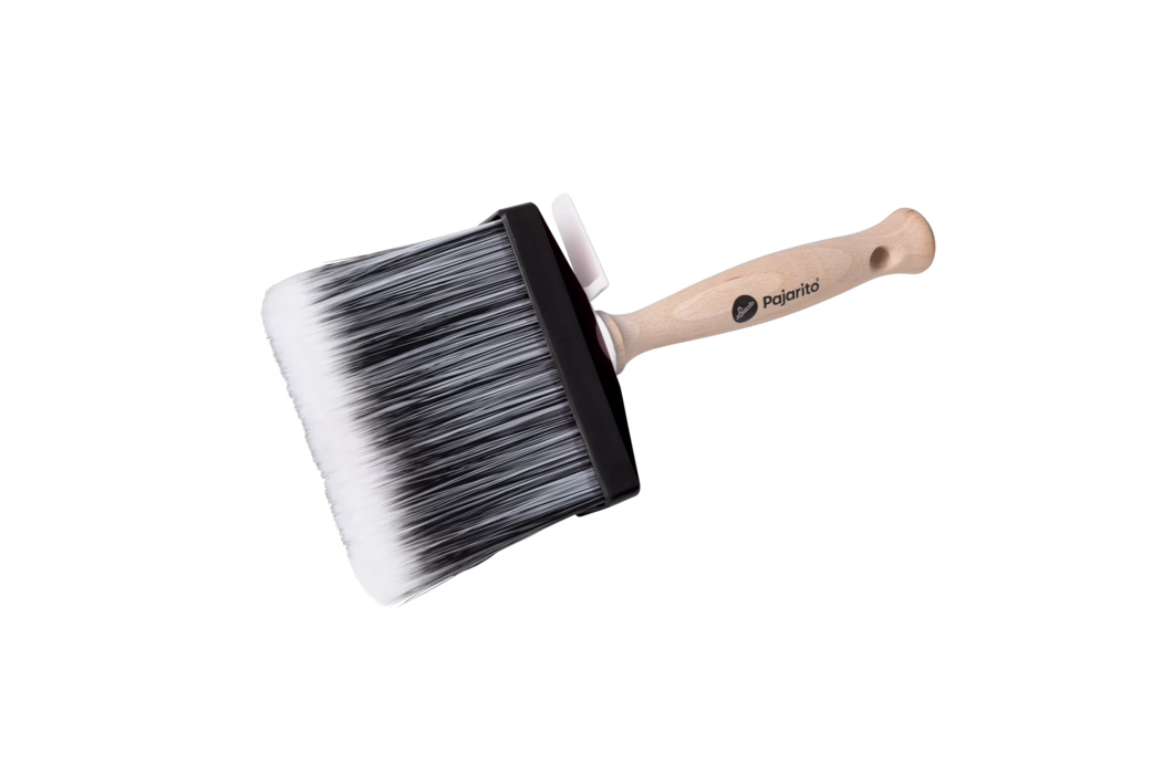 Pajarito_Dummy_Surface brush Water Maxx P-Line_179072_179073_2024-02 Ein großes, rechteckiges Malerpinsel auf weißem Hintergrund, leicht schräg fotografiert. Der Pinselkopf ist breit und dicht mit synthetischen Borsten, die an der Basis schwarz und zu den Spitzen hin weiß verlaufen; die Borsten sind gerade, gleichmäßig geschnitten und eng beieinander. Ein schwarzes Kunststoff-Ferrule hält die Borsten an einem ergonomisch geformten, hellen Buchenholzgriff mit Aufhängeloch; auf dem Griff ist das Logo 'pajarito' aufgedruckt. Nahe dem Ferrule ist eine kleine weiße Kunststoffklammer befestigt. Die gleichmäßige Ausleuchtung und weiche Schatten betonen die Struktur der Borsten und die Holzmaserung; der Pinsel eignet sich zum Auftragen von Farbe auf große Flächen wie Wände und Decken und vermittelt einen professionellen, hochwertigen Eindruck.