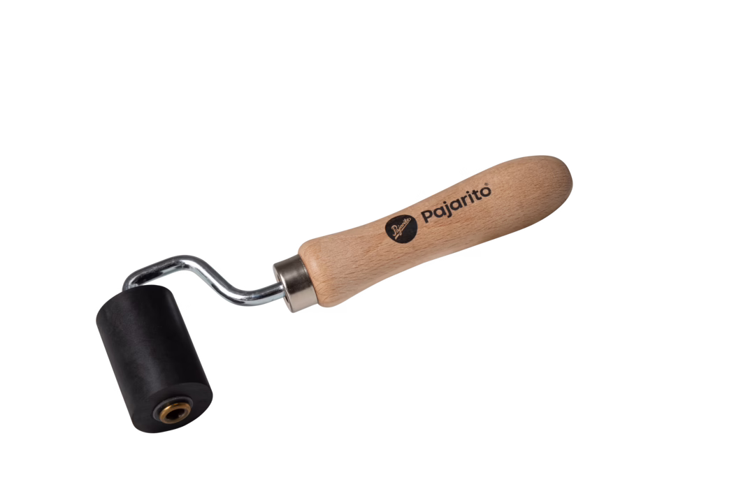 Ein kleiner Handroller mit glattem Holzgriff, auf dem "Pajarito" steht, einer verchromten gebogenen Metallachse und einer zylindrischen schwarzen Gummiwalze. Das Werkzeug dient zum Andrücken von Stößen, Glätten von Klebstoffen und Vinyl sowie zum Entfernen von Luftblasen bei Tapezier-, Bodenbelags- oder Bastelarbeiten. Auf weißem Hintergrund fotografiert, zeigt der Holzgriff Maserung und eine Metallhülse verbindet ihn mit der Walze; handliche Größe für präzise Arbeiten.