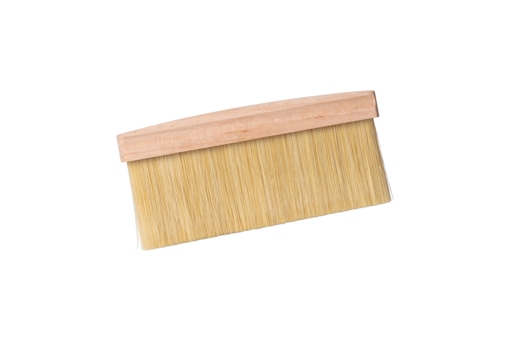 Ein breiter, flacher Pinsel mit hellem Holzgriff und dicht stehenden hellbeigen synthetischen Borsten, auf weißem Hintergrund leicht diagonal dargestellt. Der Pinsel wird meist zum Tapezieren, Abstauben oder Auftragen von Lacken verwendet; die langen, dicht angeordneten Borsten sind an einem einfachen, unbehandelten Holzrücken befestigt.